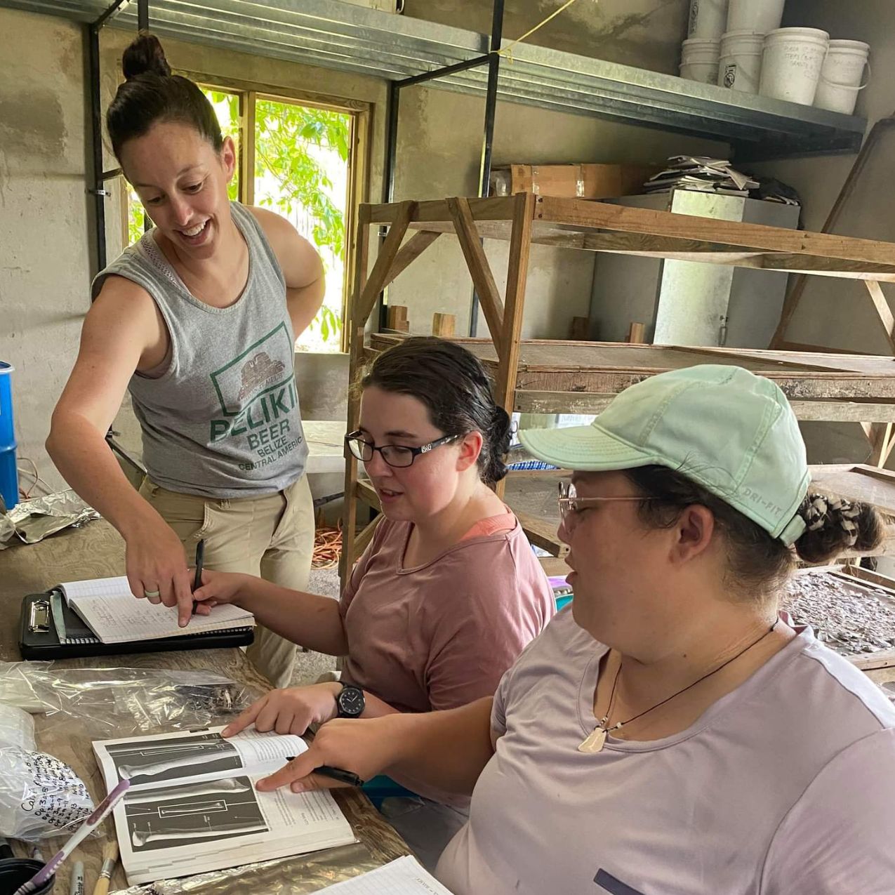 Professor Mink works with two students at a field location inside a cabin. The group is looking at texts.