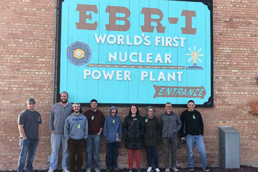 a class field trip to INL, a group of students stand in front of a nuclear building sign.