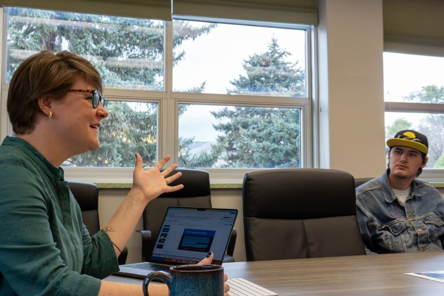 Sarah Robey sits at a conference table with a student. She gestures and smiles as she teaches.