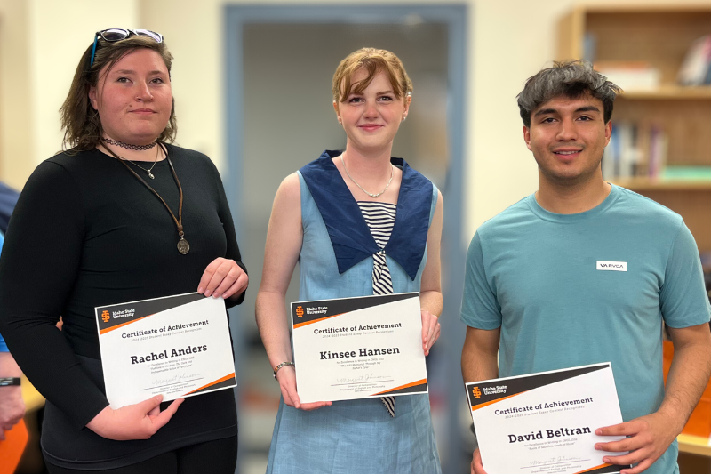 three students hold certificates of achievement