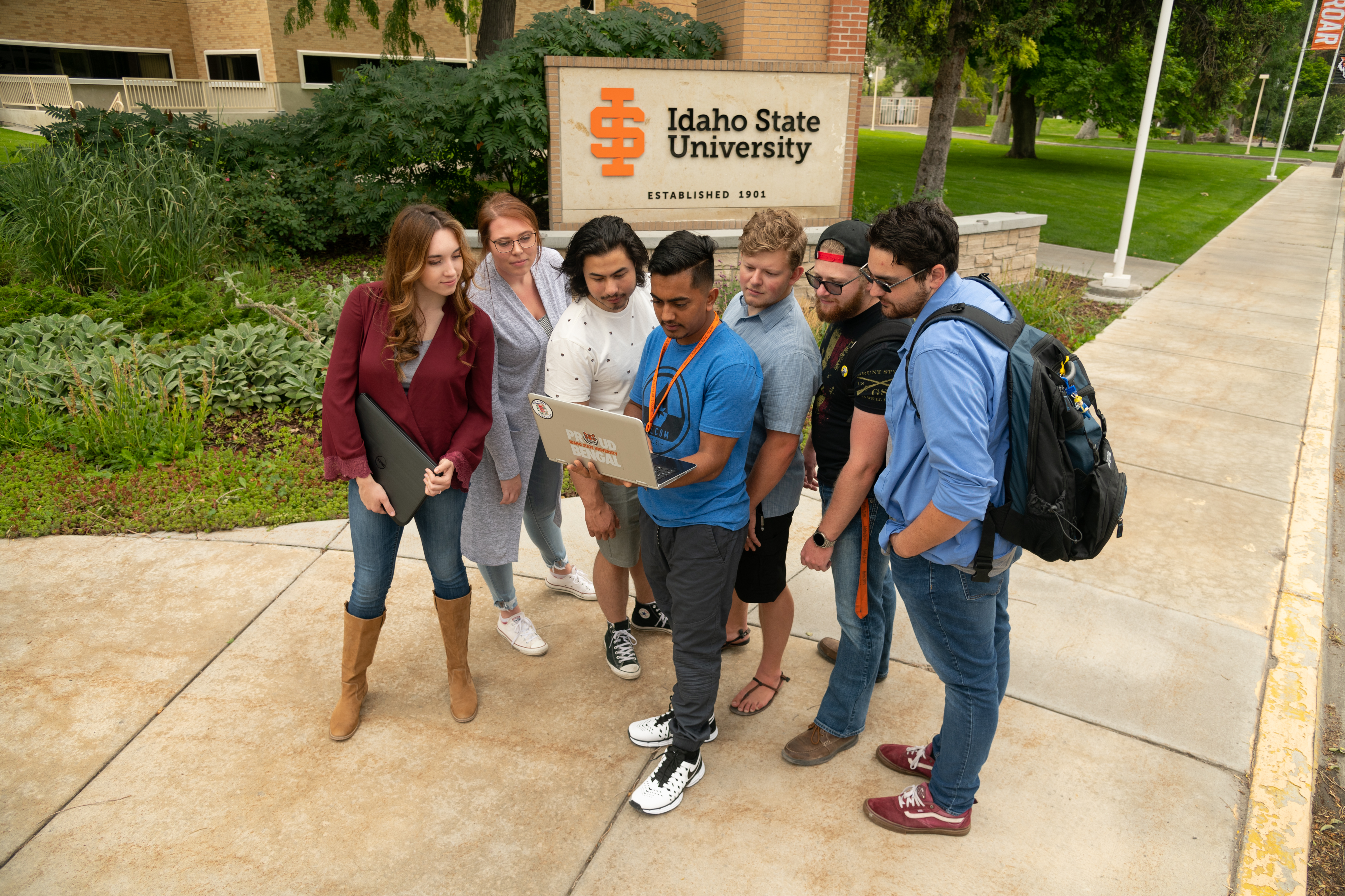 Group of students looking at a laptop outdoors in front of an ISU sign.