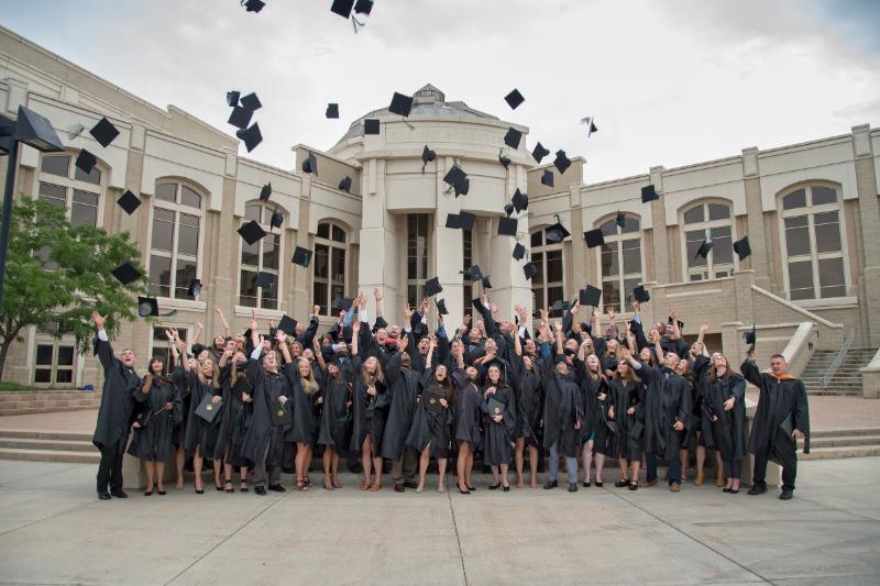 graduates throwing their hats in the air in front of building