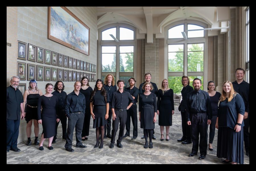 The ISU chamber choir members stand in the lobby of the Stephen's Performing Arts Center. They are all dressed in black and smiling.