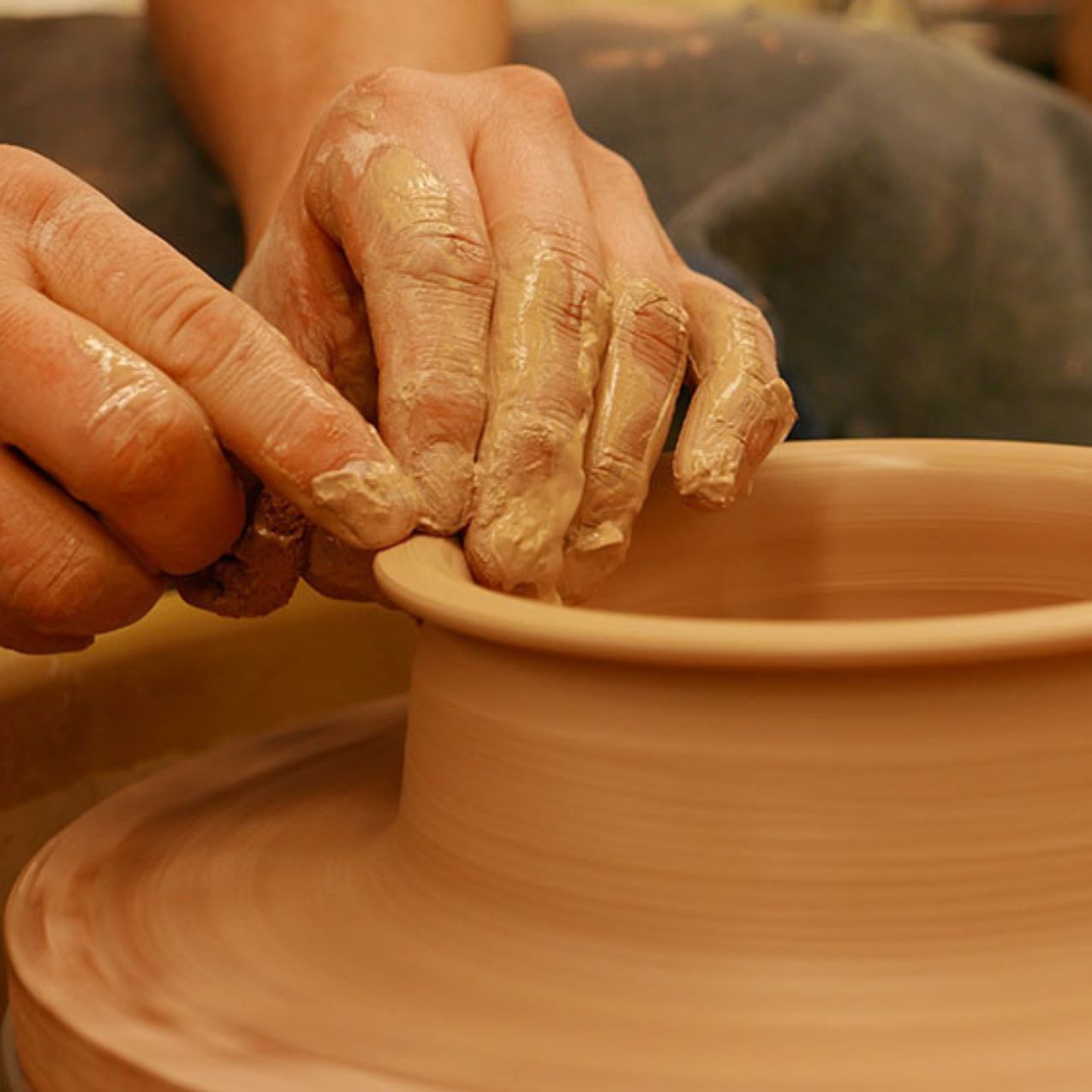 Close up of clay on a clay throwing wheel with hands manipulating the clay