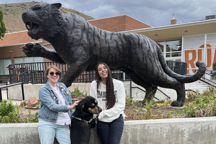 Joules and Julia stand in front of the Bengal statue with a black lab dog between them