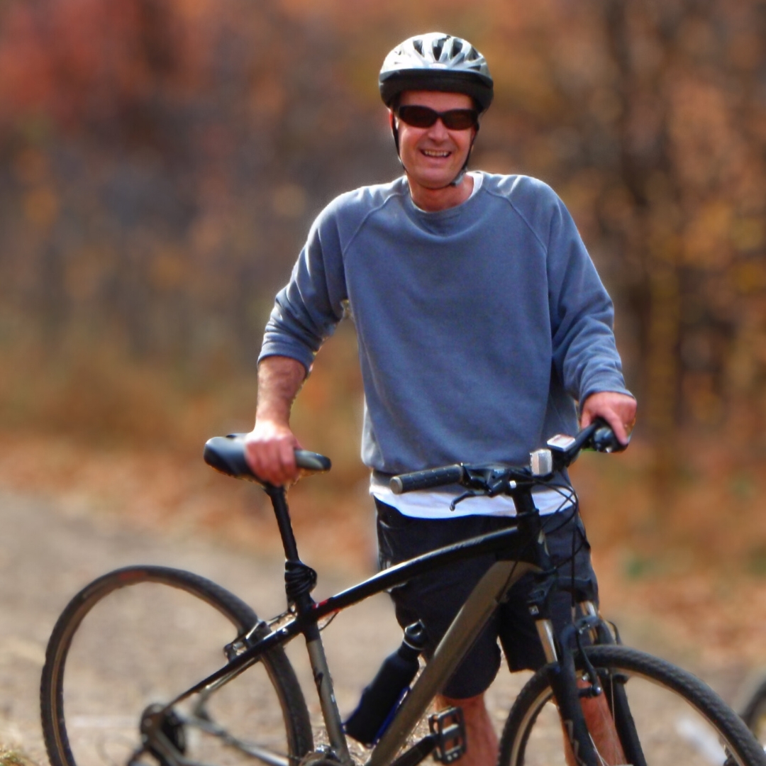Mark McBeth stands next to a mountain bike with fall foliage in the background