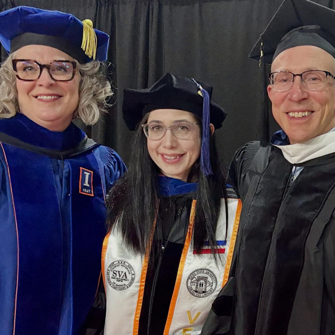 Mel, Zink, and Klein in academic regalia, two hugging and one smiling beside them.