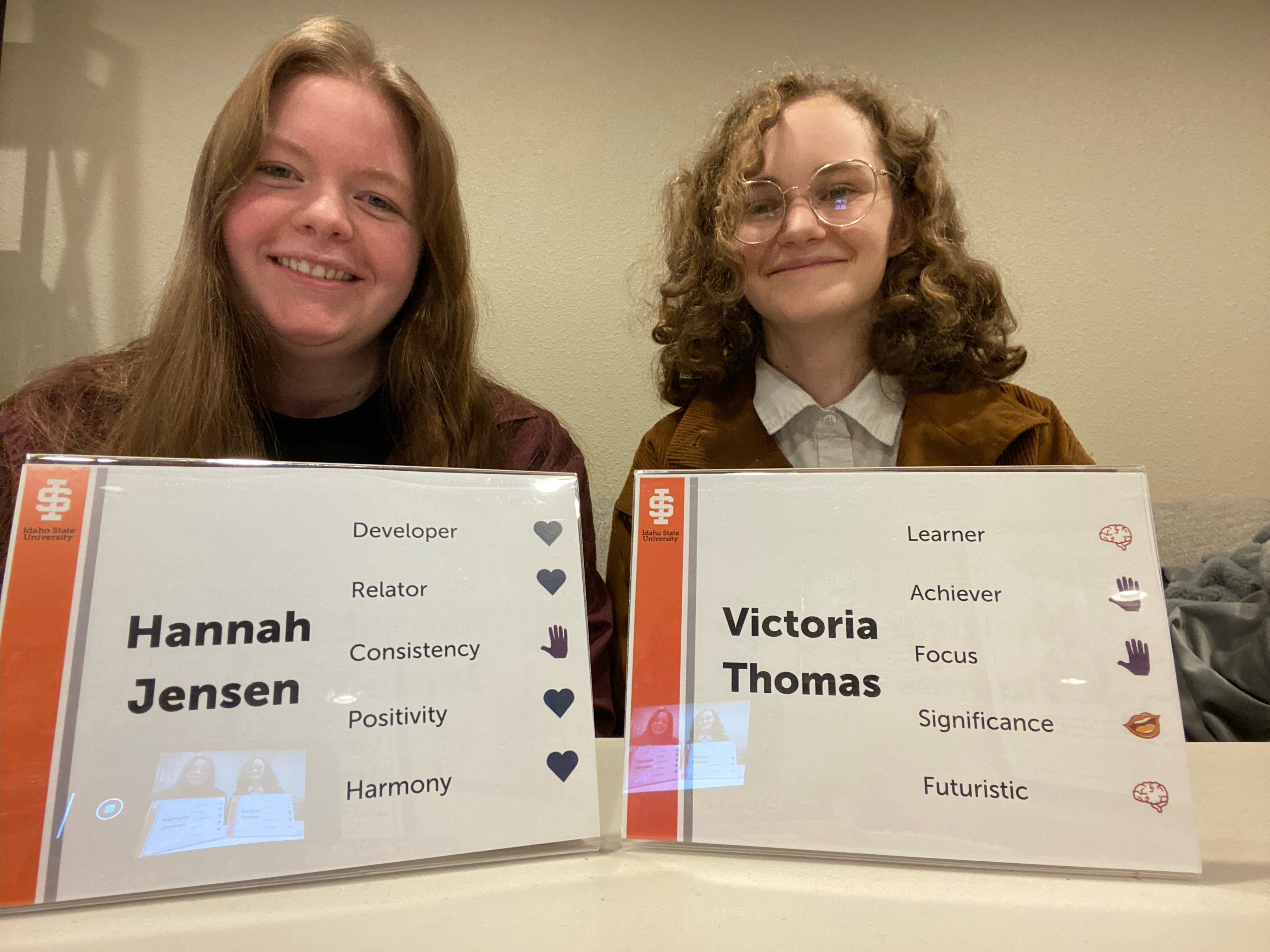 Two students holding name signs with traits and icons.