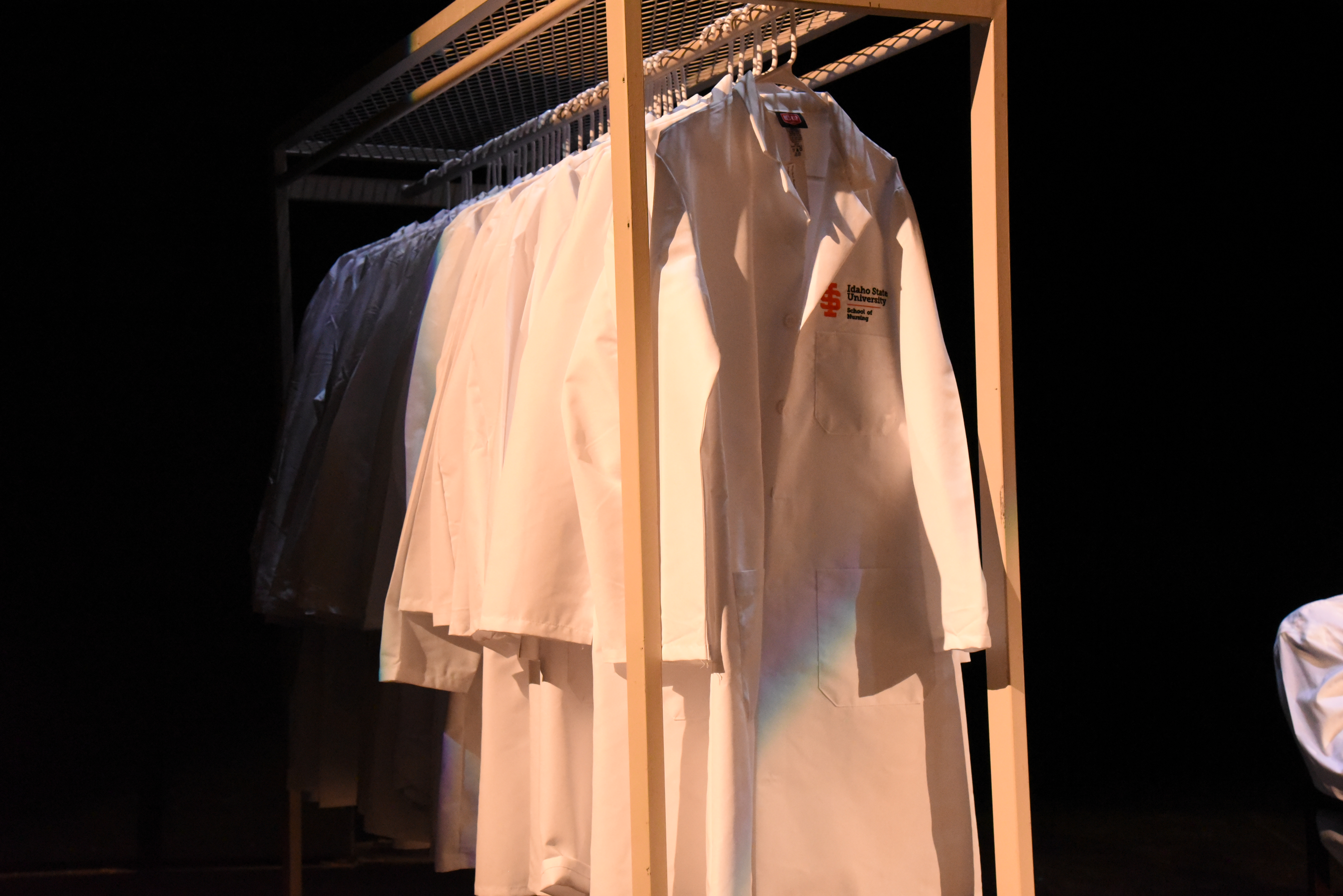 A group of white coats hanging on a garment rack. The embroidery on the chest says 