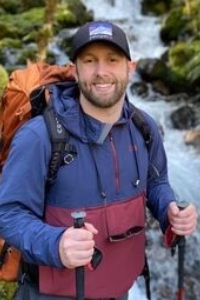 Nicholas Patton smiles and poses while backpacking, hiking sticks in each hand