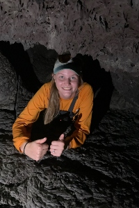 Ashley Butterworth crawling happily toward the camera in a low ceiling cave