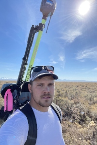 Brooks Meyers wearing a device on his back outside with sagebrush, likely looking for grouse