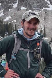 David Cavell in the outdoors with a back pack in front of a mountain