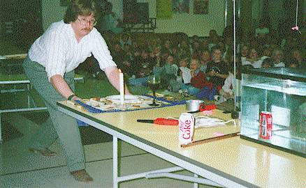 Dr. Shropshire demonstrates the principle of inertia for elementary students by pulling a place mat from under a plate and candle