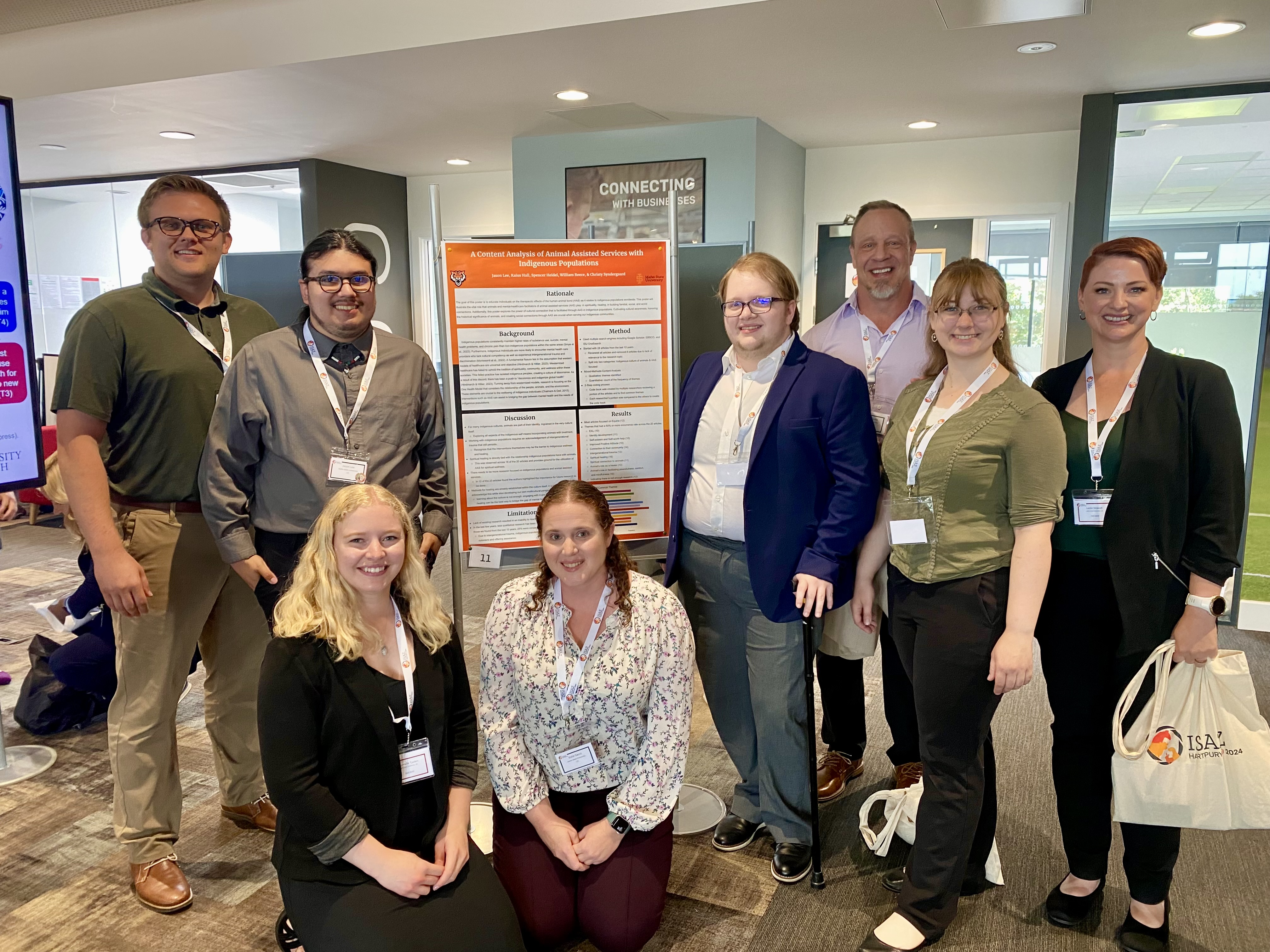 Eight people standing around a large orange and white posterboard with words on it. The poster is for presenting research related to ROAR.