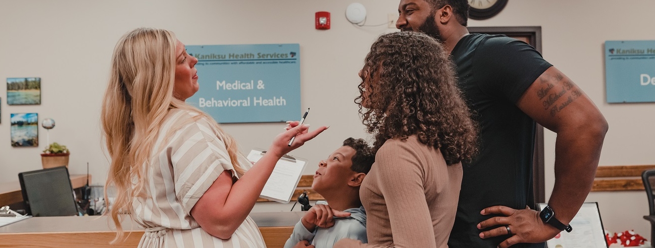 A CHW Apprentice speaking to a family of three in front of a health clinic desk.