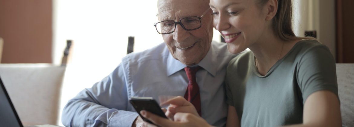 A young woman helping an elderly man with a mobile phone.