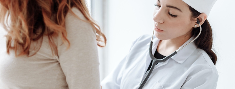 A health professional using a stethoscope on a patient's back