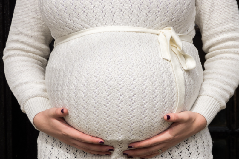 Belly of pregnant woman in white knit dress