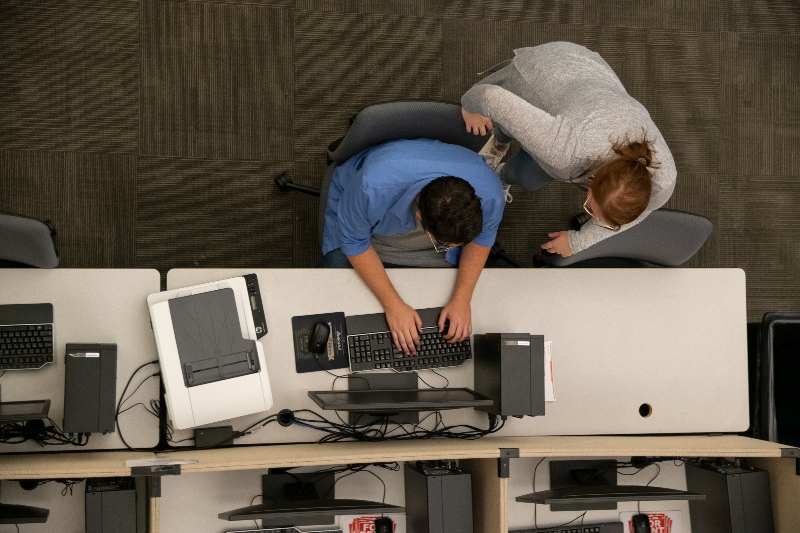 A student working on a computer receiving help from another person.