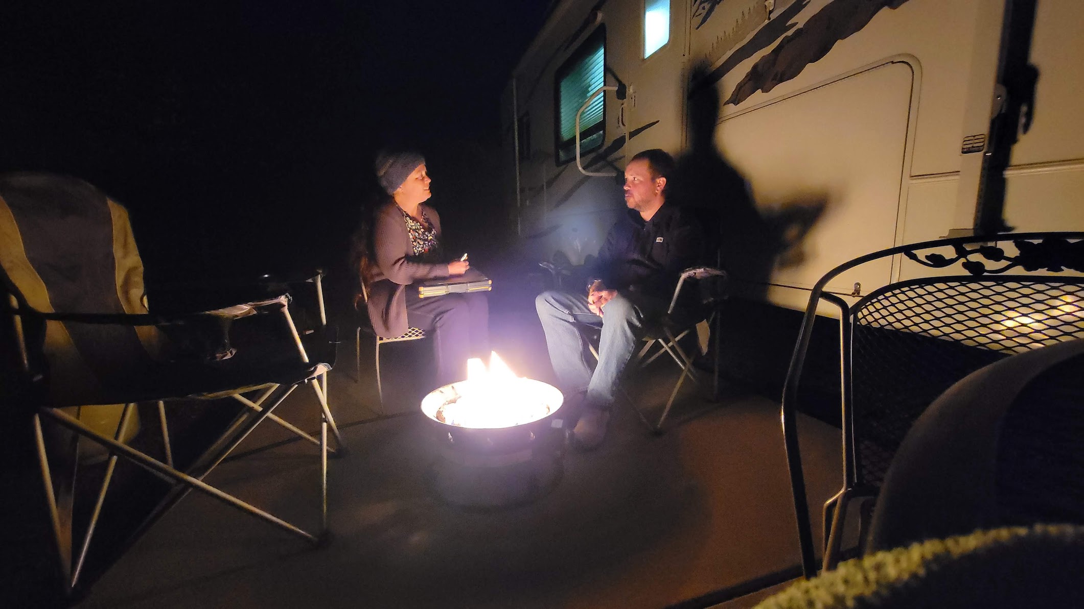 A researcher sits by a campfire outside of an RV at a remote site as part of a PhD research project