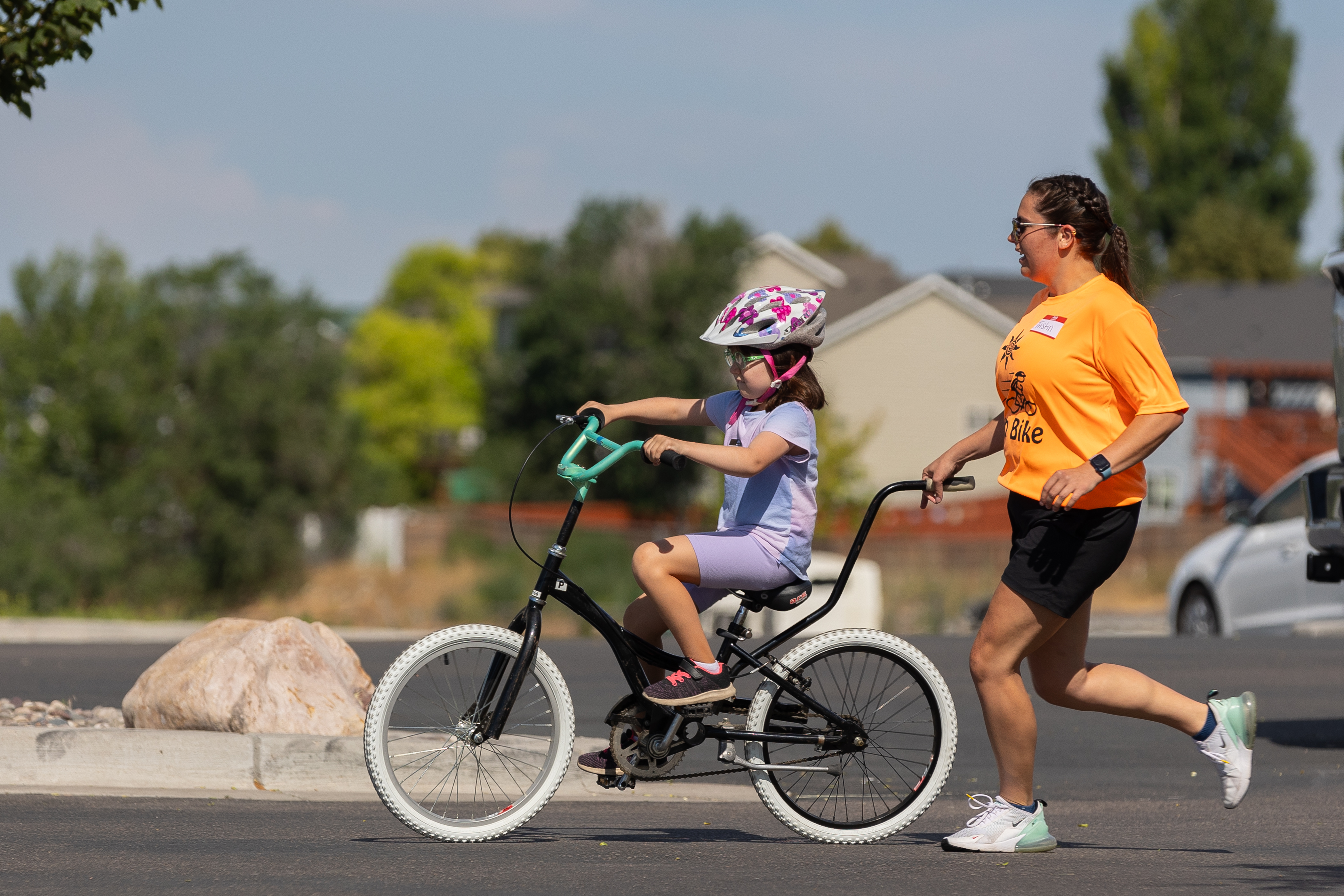An OT student helps a child ride a bike by holding a stabilizing handle and jogging behind the bike.
