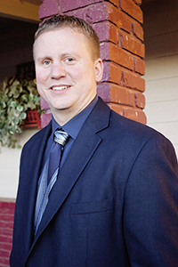 Ryan Gerulf, Director of Development for the KDHS, poses for a headshot in a dark suit outside of a brick building