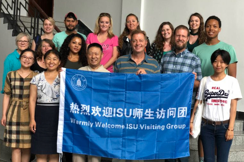 A group of ISU students and students from China's Sichuan University pose with ISU professors of counseling Dr. David Kleist and Dr. Steven Moody holding a welcome flag