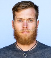 Faculty member Luke Nelson headshot; blue t-shirt and beard