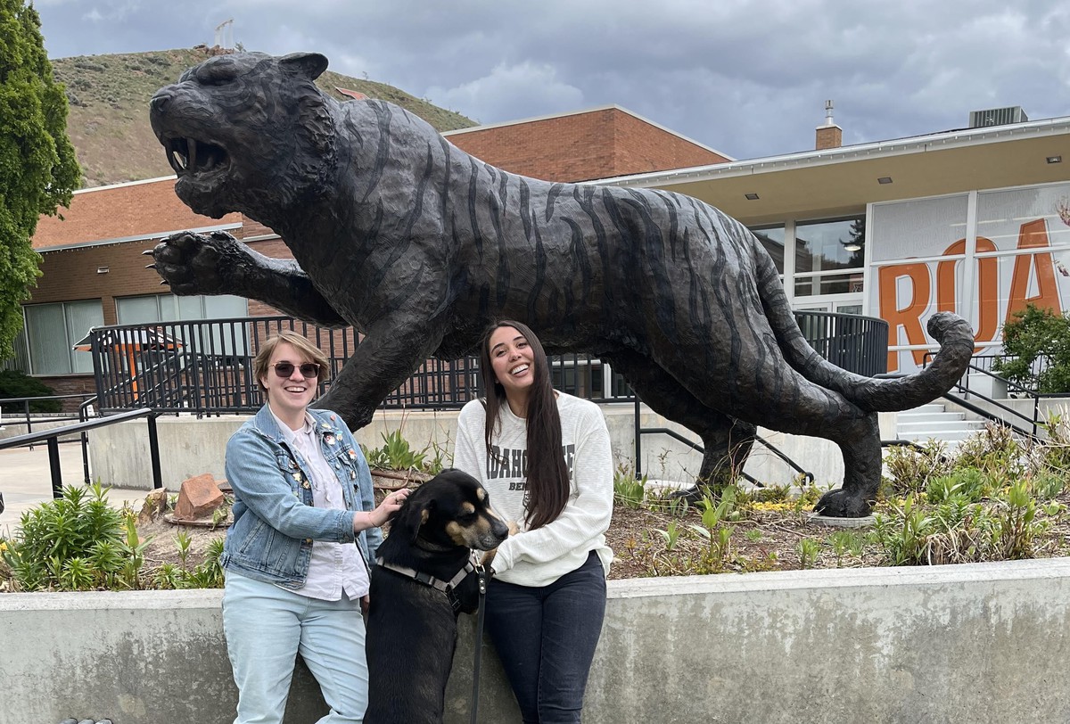 Joules Emerson and Julia Duran pose in front of the Bengal Tiger statue on campus with a dog