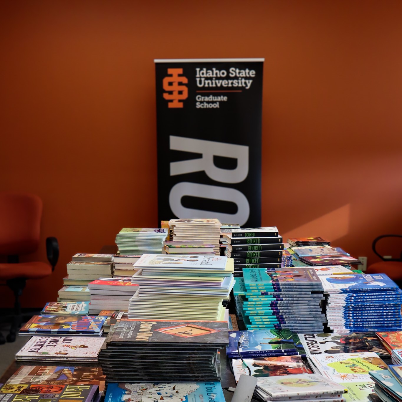 stacks of books donated for the Graduate School book drive, with ROAR banner in background