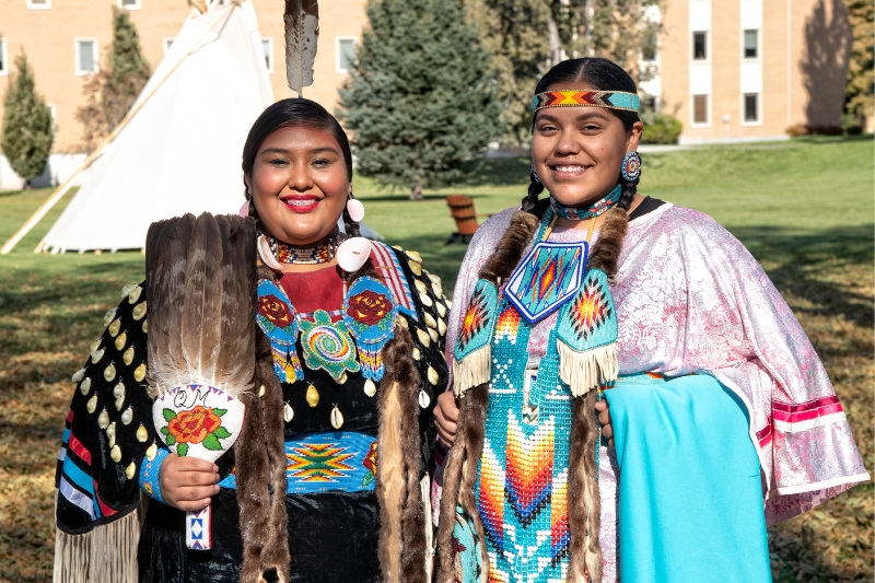 Two students stand in traditional Native American dress