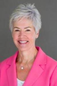 A woman with short white and grey hair, light skin tone. She is wearing a bright pink suit jacket and a white suit
