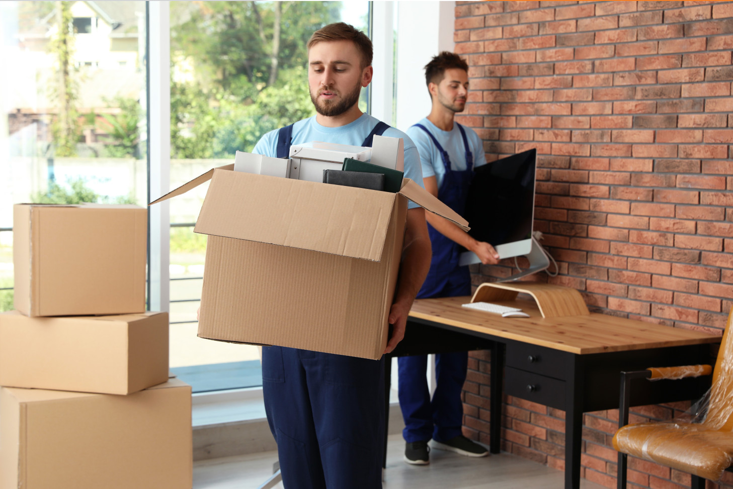 A man lifts a moving box while another man lifts a monitor