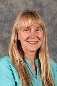 A fair skin tone woman with blonde hair. She is wearing a seafoam shirt and is smiling.