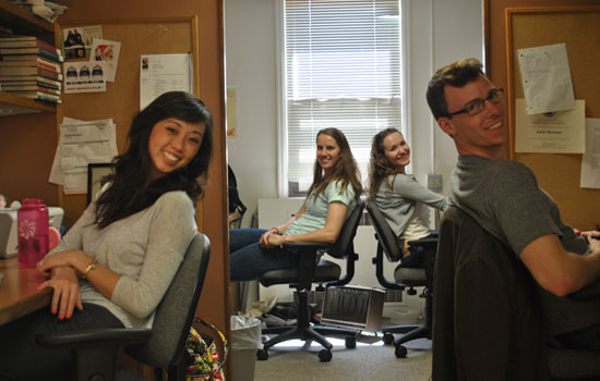 students sit at desks in desk chairs leaning backward and smiling at the camera