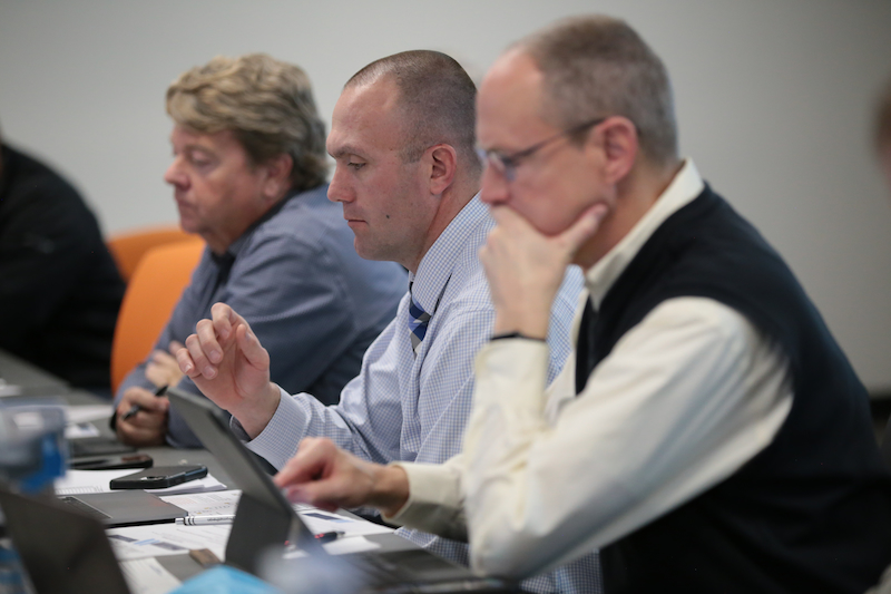 3 men sitting at a table in a meeting looking at their tablets