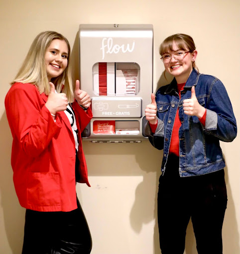 Two girls in front of a period products dispenser