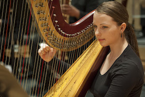 A picture of a woman playing a harp for the symphony.