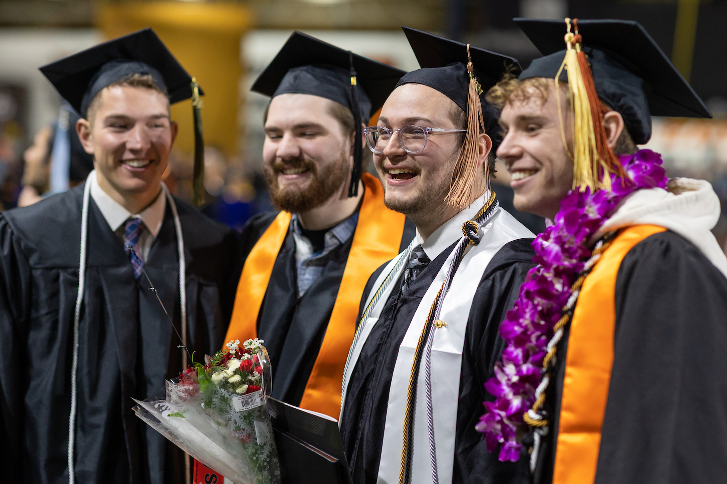 Four men in graduation regalia pose for a photo