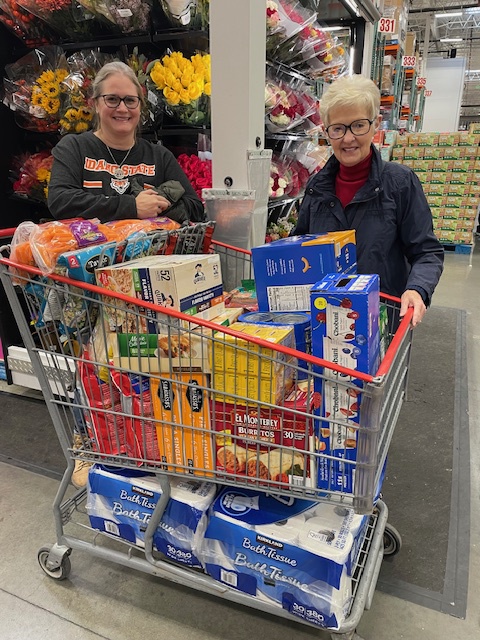 Two women stand by a full shopping cart