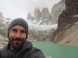 Photo of Ben Crosby with a glacial lake and mountains in the background. 