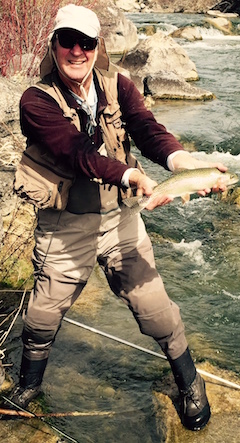 Photo of an angler in waders standing in a stream holding a big trout.
