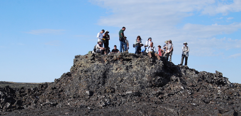 Photo of six ISU and NASA researchers standing on a ridge of lava rock with blue sky in background. 