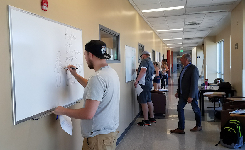 Photo of business students in hallway writing on eraser boards