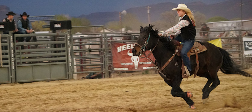 Makayal Boots in action riding here black horse in the rodeo arena.