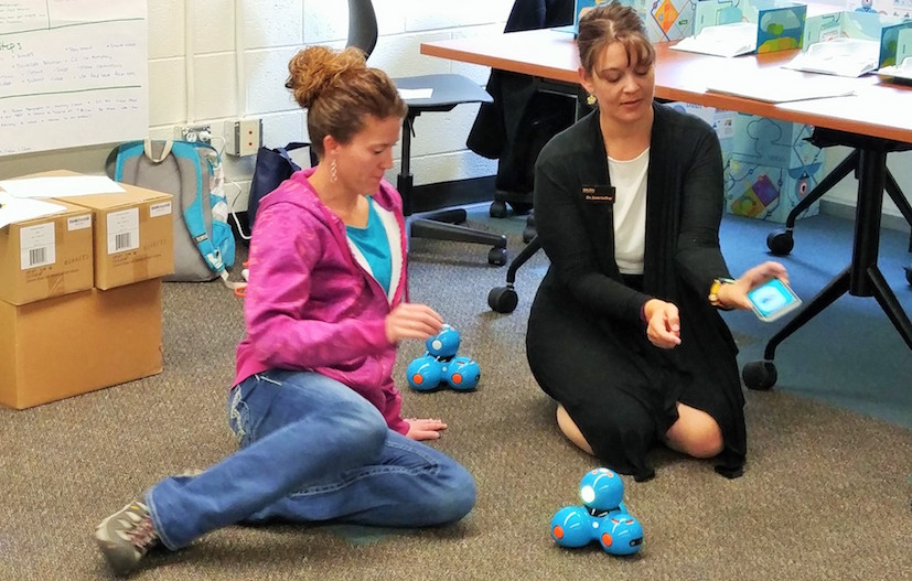 Photo of a young female student on floor with faculty member using a robot. 