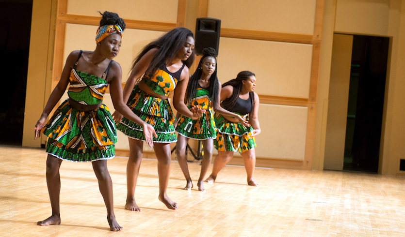 A scene of five dancers from the 2016 Africa Night performing onstage with floral-patterned dresses on. 