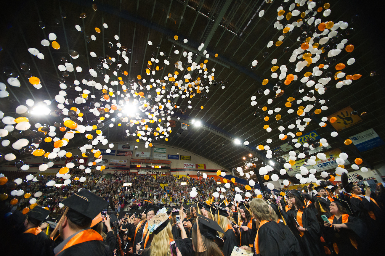 Students on floor of Holt Arena at 2019 commencement with balloons falling down. 