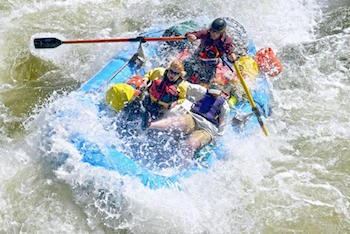Photo of raft with three passengers splashing through whitewater rapids